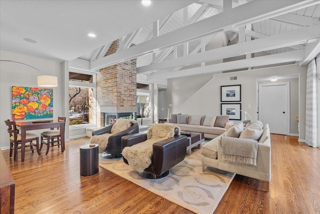 living room featuring high vaulted ceiling, a brick fireplace, hardwood / wood-style floors, and beam ceiling