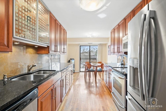 kitchen featuring sink, light hardwood / wood-style flooring, dark stone countertops, stainless steel appliances, and decorative backsplash