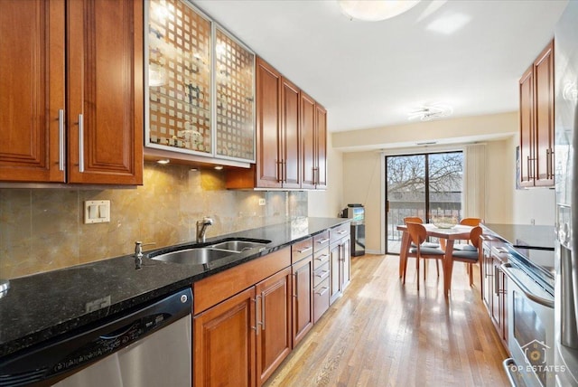 kitchen with appliances with stainless steel finishes, sink, dark stone countertops, decorative backsplash, and light hardwood / wood-style flooring