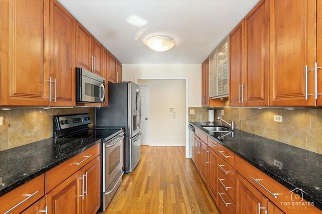 kitchen with appliances with stainless steel finishes, sink, light hardwood / wood-style flooring, and dark stone countertops