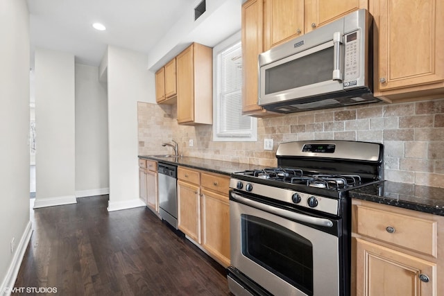 kitchen with dark stone countertops, decorative backsplash, light brown cabinetry, and appliances with stainless steel finishes