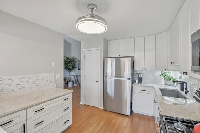 kitchen featuring white cabinets, light stone countertops, sink, and stainless steel fridge