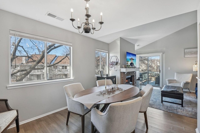 dining area with an inviting chandelier, wood-type flooring, a brick fireplace, and plenty of natural light