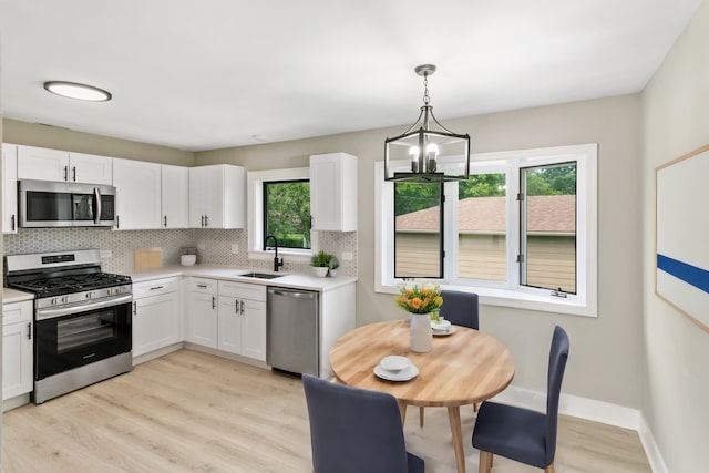 kitchen with stainless steel appliances, white cabinetry, and decorative light fixtures