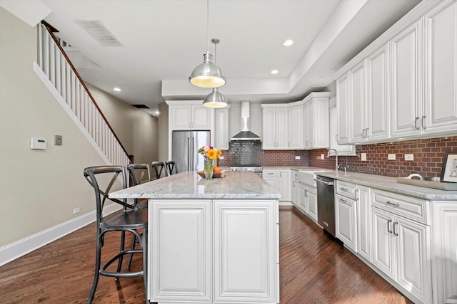 kitchen featuring wall chimney exhaust hood, a kitchen island, white cabinets, and stainless steel appliances