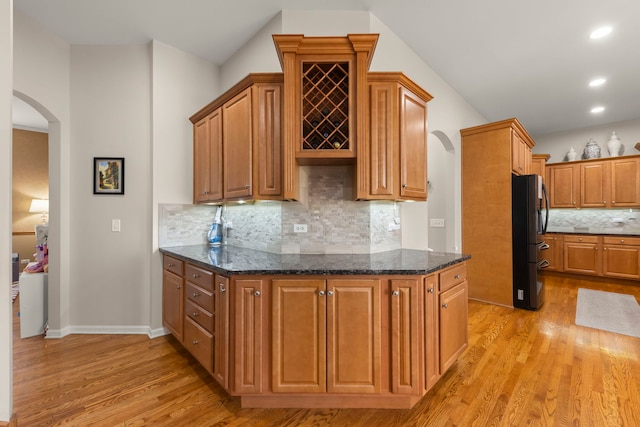 kitchen with dark stone countertops, backsplash, light wood-type flooring, and refrigerator