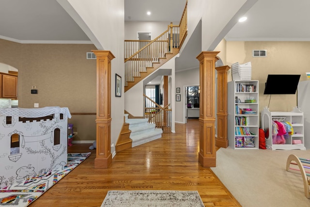 entrance foyer featuring ornate columns, crown molding, a towering ceiling, and light hardwood / wood-style floors