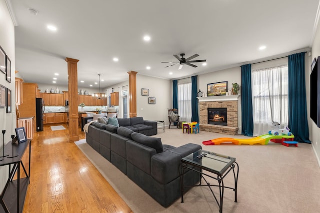 living room featuring ornate columns, crown molding, a brick fireplace, ceiling fan, and light hardwood / wood-style floors