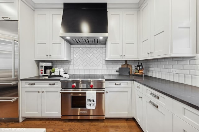 kitchen with white cabinets, premium appliances, decorative backsplash, and wall chimney range hood