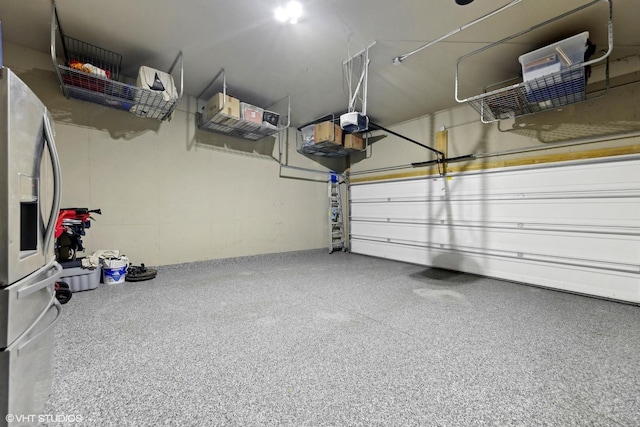 garage with a garage door opener and stainless steel refrigerator with ice dispenser