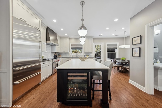 kitchen featuring wine cooler, pendant lighting, built in fridge, and wall chimney range hood