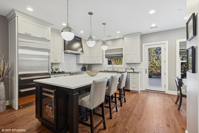 kitchen with pendant lighting, wall chimney range hood, white cabinetry, a center island, and built in fridge