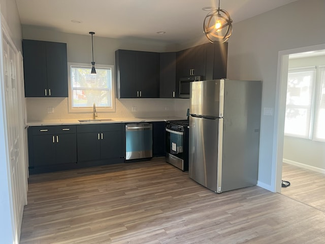 kitchen with decorative light fixtures, decorative backsplash, sink, light hardwood / wood-style flooring, and stainless steel appliances