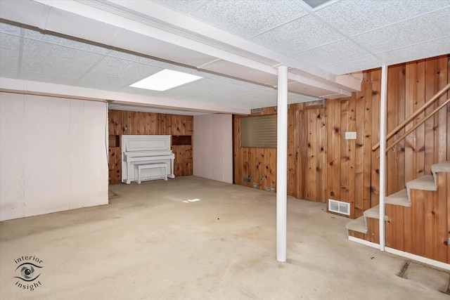 basement with a paneled ceiling, carpet floors, and wood walls