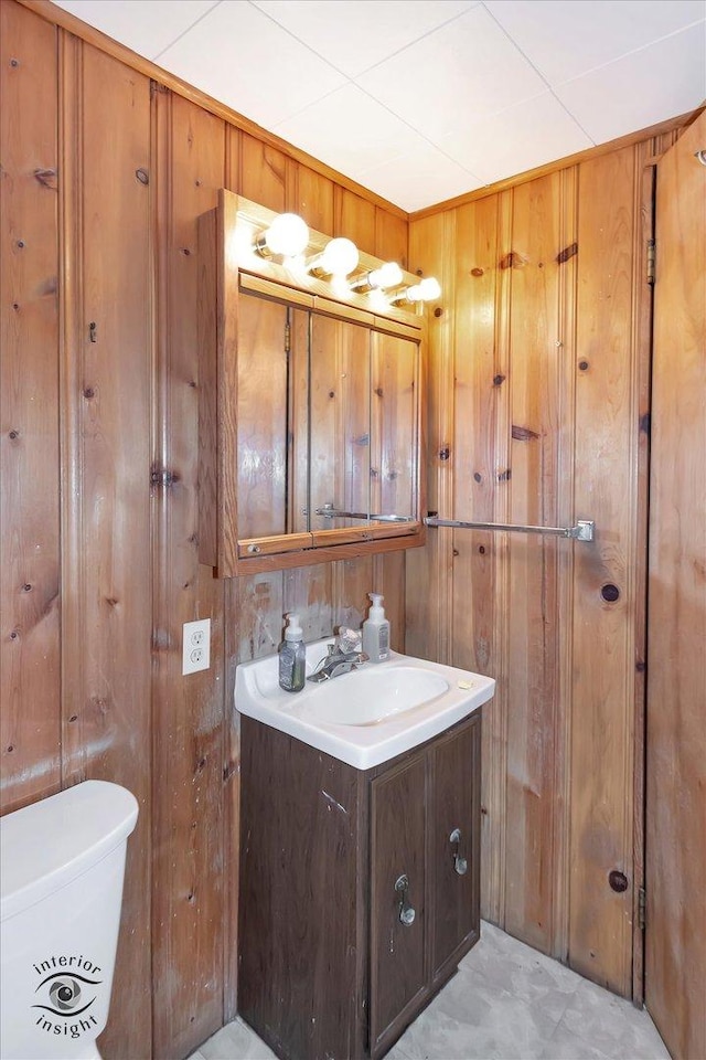 bathroom featuring vanity, wooden walls, and toilet