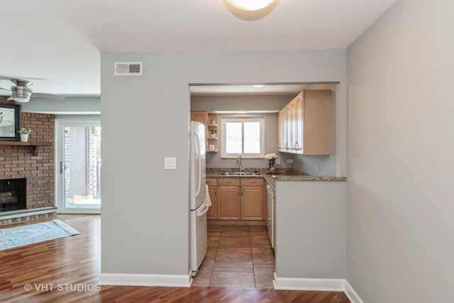 kitchen with light brown cabinetry, sink, hardwood / wood-style flooring, white fridge, and a brick fireplace