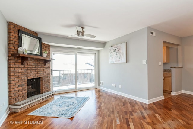 unfurnished living room featuring hardwood / wood-style flooring, ceiling fan, and a brick fireplace