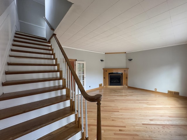 stairway featuring crown molding, a fireplace, and hardwood / wood-style floors