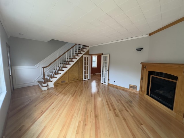 unfurnished living room with crown molding, light hardwood / wood-style floors, and french doors