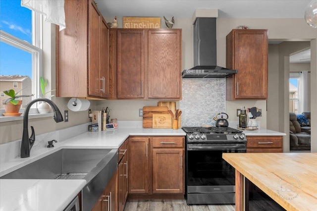 kitchen featuring stainless steel range with gas cooktop, butcher block counters, sink, wall chimney range hood, and light hardwood / wood-style flooring