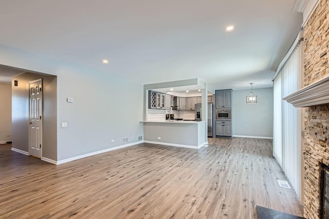 unfurnished living room featuring light hardwood / wood-style flooring and a stone fireplace