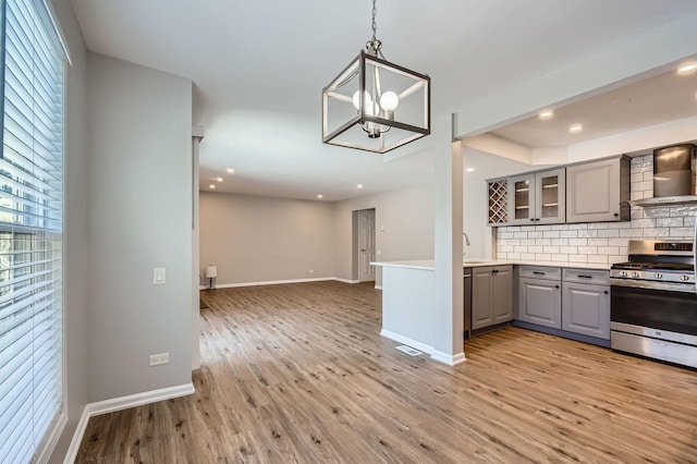 kitchen featuring wall chimney range hood, decorative backsplash, stainless steel gas range oven, hanging light fixtures, and gray cabinetry