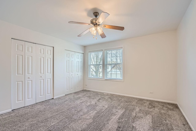 unfurnished bedroom with ceiling fan, carpet floors, and two closets