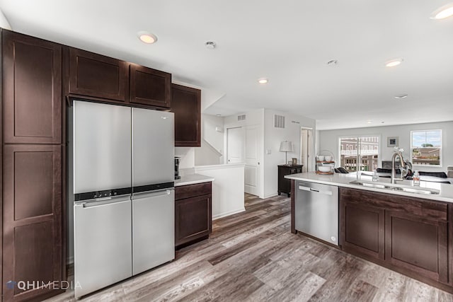 kitchen with appliances with stainless steel finishes, dark brown cabinets, light hardwood / wood-style flooring, and sink