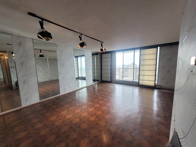 empty room with parquet flooring, track lighting, and a textured ceiling