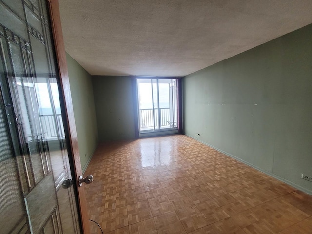 empty room with parquet floors, floor to ceiling windows, and a textured ceiling