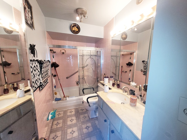 full bathroom with vanity, toilet, combined bath / shower with glass door, and tile walls