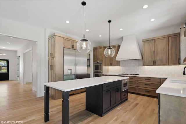 kitchen with sink, custom exhaust hood, decorative light fixtures, light wood-type flooring, and stainless steel appliances