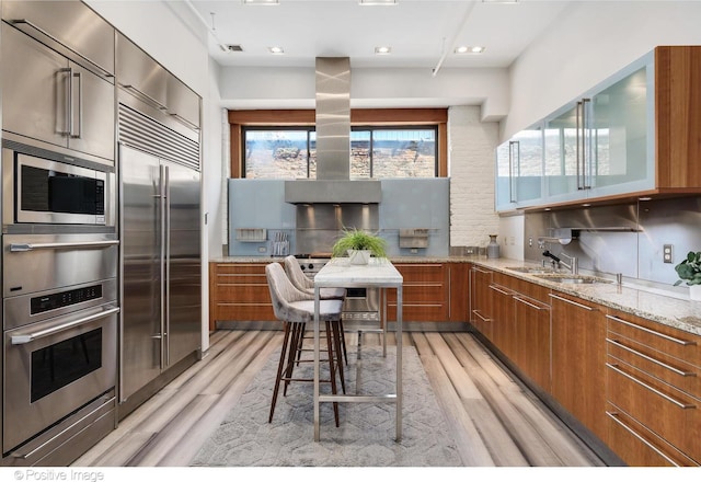 kitchen featuring light hardwood / wood-style floors, decorative backsplash, light stone countertops, built in appliances, and sink