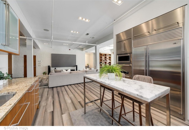 kitchen featuring light stone countertops, light hardwood / wood-style flooring, and built in appliances