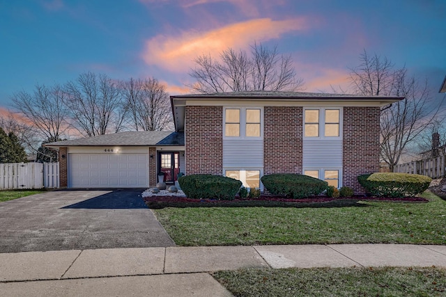 split level home with brick siding, fence, a lawn, driveway, and an attached garage