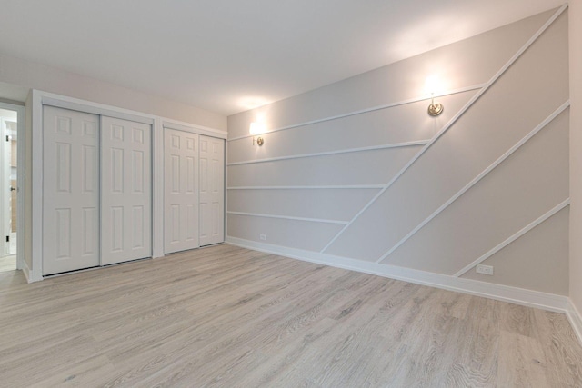 unfurnished bedroom with two closets and light hardwood / wood-style flooring