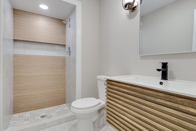 bathroom with toilet, tile patterned flooring, a tile shower, and vanity