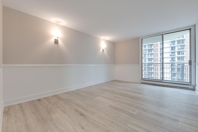 empty room with a wealth of natural light, a baseboard radiator, and light hardwood / wood-style flooring