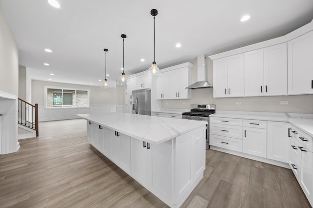 kitchen with pendant lighting, appliances with stainless steel finishes, a kitchen island, wall chimney range hood, and white cabinetry