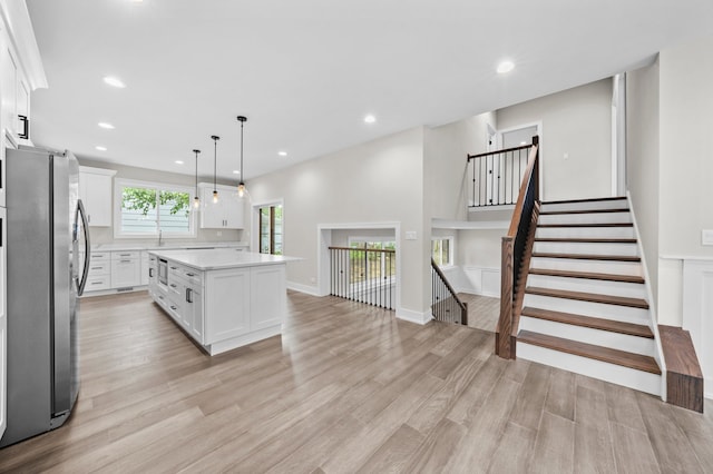 kitchen featuring white cabinetry, light hardwood / wood-style floors, stainless steel fridge, decorative light fixtures, and a kitchen island