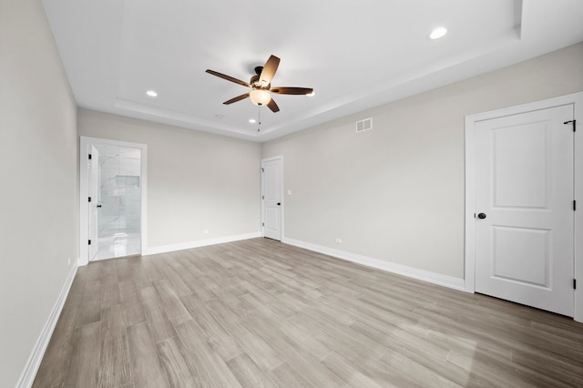 spare room with ceiling fan, light wood-type flooring, and a tray ceiling