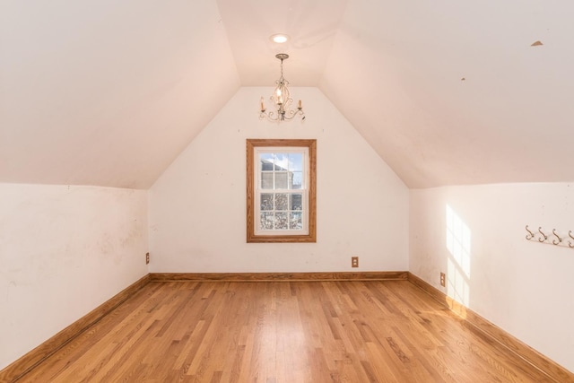 additional living space with light wood-type flooring, a notable chandelier, and vaulted ceiling