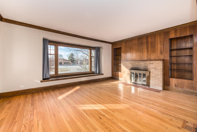 unfurnished living room featuring built in shelves, light hardwood / wood-style flooring, ornamental molding, and a fireplace