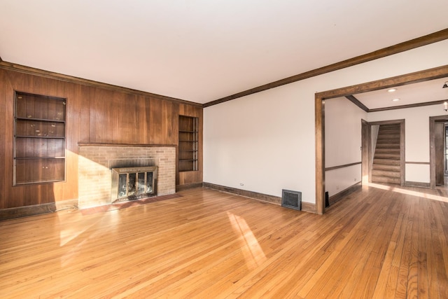 unfurnished living room with light wood-type flooring, built in features, crown molding, and a fireplace