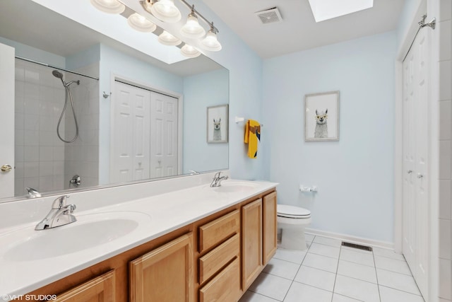 bathroom featuring tiled shower, toilet, a skylight, vanity, and tile patterned flooring