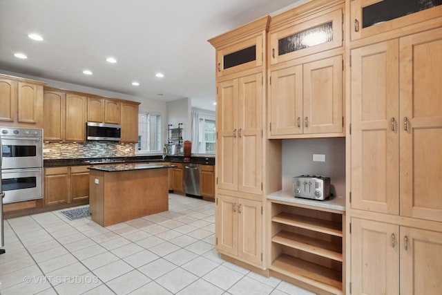 kitchen featuring light tile patterned flooring, appliances with stainless steel finishes, backsplash, a center island, and light brown cabinets