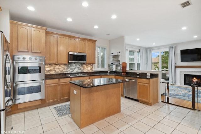 kitchen with sink, light tile patterned floors, dark stone countertops, appliances with stainless steel finishes, and a kitchen island