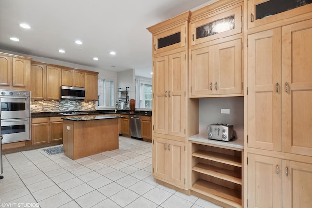 kitchen featuring light tile patterned floors, appliances with stainless steel finishes, a center island, decorative backsplash, and light brown cabinets