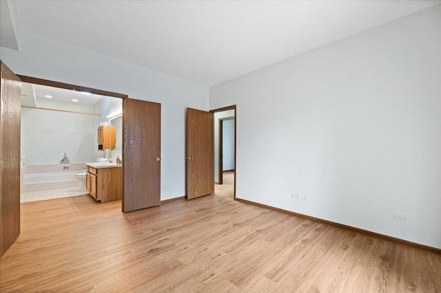 unfurnished bedroom featuring light wood-style flooring, baseboards, and ensuite bathroom