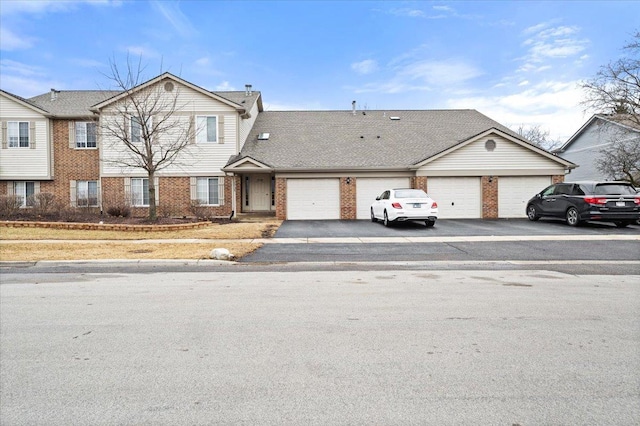 multi unit property featuring a shingled roof, brick siding, driveway, and a garage